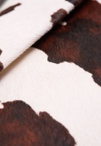 Kůže z kravského chlupu s vzorem velkých hnědých a bílých skvrn, s měkkým a texturovaným povrchem.