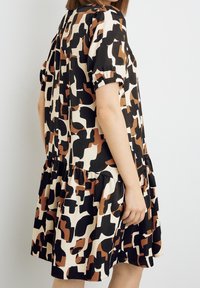 Korte mouw jurk in een zwart, crème en bruin abstract patroon. Bevat een gelaagde rok en elastische mouwen voor een ontspannen pasvorm.