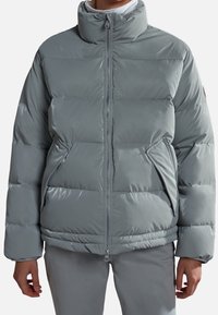 Lys grå pufferjakke med høj krave, quiltet design og lynlås. Har sidelommer og en glat, blank overflade.