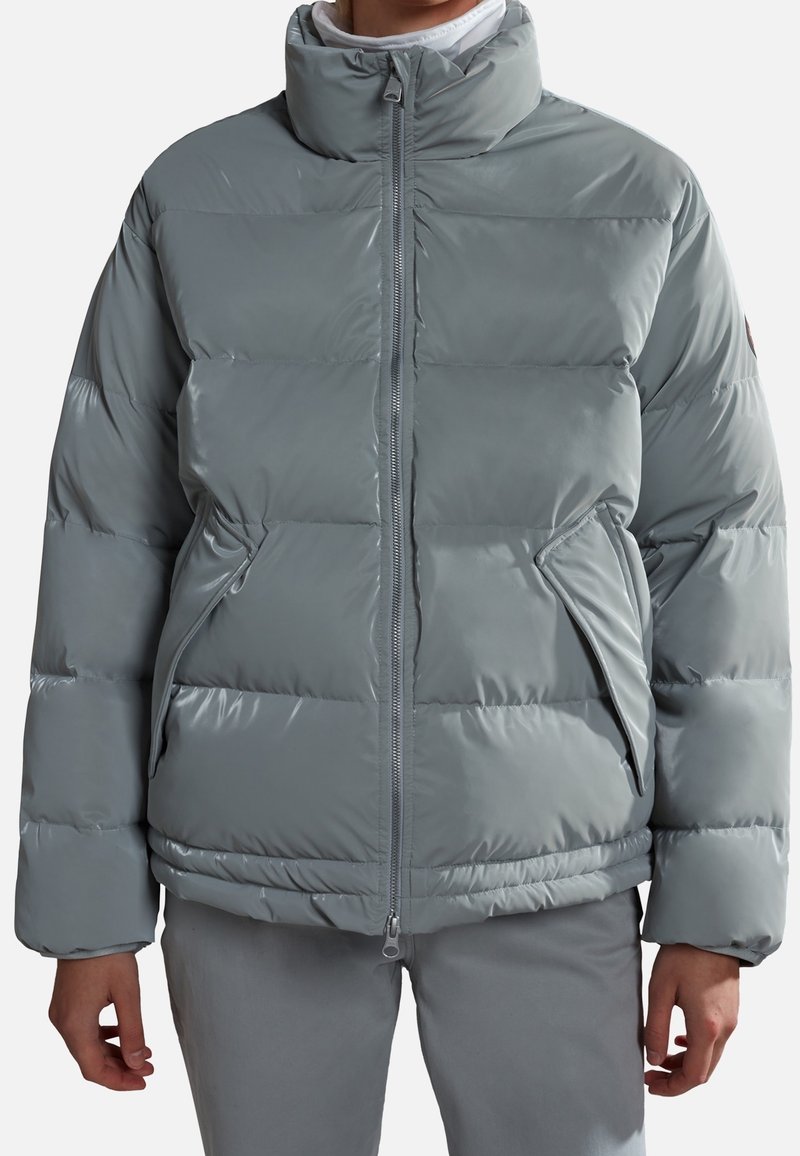 Lys grå pufferjakke med høj krave, quiltet design og lynlås. Har sidelommer og en glat, blank overflade.