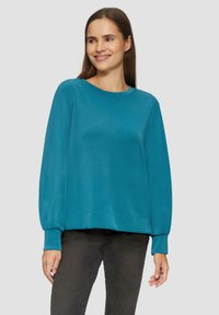 Teal sweatshirt met een ronde halslijn, relaxed fit en lange mouwen. Zacht materiaal met ribbelmanchetten en onderrand, gedragen met donkere jeans.