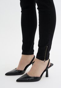 Juodi odiniai slingback aukštakulniai batai su smailiu pirštu ir stiletto kulnu. Tekstūruota juostelė gale, derinama su juodais siaurais džinsais su užtrauktukais.
