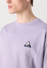 Lys lavendel bomulds T-shirt med et trekantet broderet mærke med "BOSS" tekst. Rund halsudskæring og afslappet pasform.