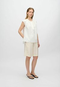 Top bianco senza maniche con scollo arricciato abbinato a pantaloni corti beige chiaro con un delicato motivo floreale. Sandali a infradito neri.