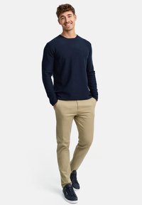 Camicia a maniche lunghe blu navy, pantaloni chinos color sabbia e sneakers blu navy. La camicia ha un collo a girocollo; i pantaloni sono aderenti con tasche laterali.