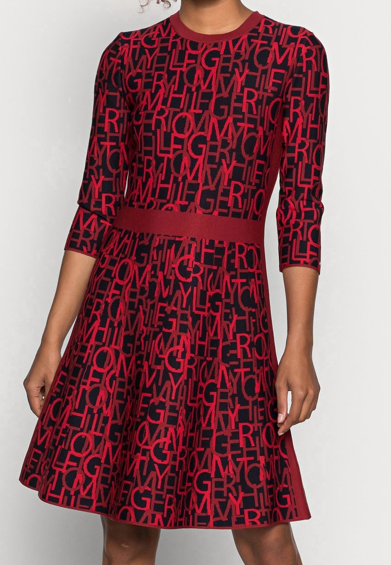 Robe rouge et noire longueur genou avec manches trois-quarts, présentant un motif audacieux de lettres sur toute la surface et une ceinture unie.