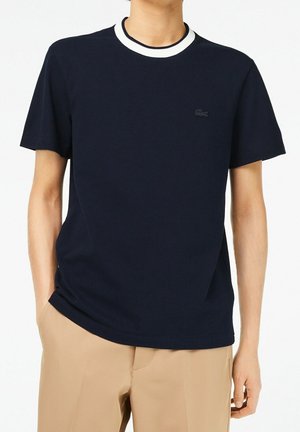 Navy blue cotton t-shirt with a white, ribbed collar. Features a small, embossed logo on the chest and short sleeves. Smooth texture.