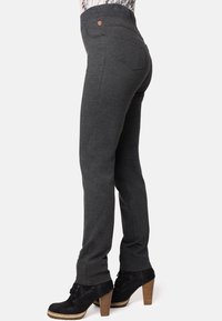 Pantalones ajustados grises con cintura alta, tejido texturizado, dos bolsillos traseros y un pequeño detalle de logo. Llevados con botas de tacón negras.