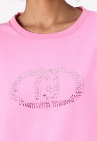T-shirt en coton rose avec un design de logo ton sur ton orné de strass transparents et roses à l'avant. Encolure classique.