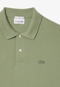 Polo shirt verde chiaro realizzato in tessuto testurizzato, con colletto a punta, patta con due bottoni e logo Lacoste ricamato sul petto.
