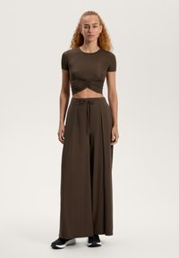 Top scurt maro cu detaliu pliat în față, asortat cu pantaloni largi maro. Ținuta are o textură moale și netedă și o croială lejeră.