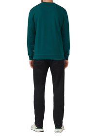 Felpa teal con maniche lunghe e collo rotondo, realizzata in materiale morbido. Indossata con pantaloni neri e sneakers bianche, vista da dietro.