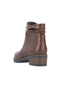 Bottine en cuir brun avec un design flou, bout rond et un talon empilé avec des accents en bois. Surface lisse avec un léger éclat.