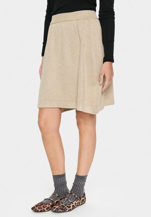 Beige a-line skirt with elastic waistband, made of soft fabric. Features side pleats and a hemline at mid-calf length. Paired with printed flats.