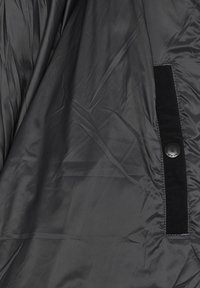 Zwart gequilt stof met een gladde textuur, voorzien van een knoopsluiting en een zwarte suède accent op de binnennaad.