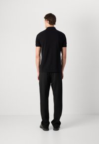 Polo noir à manches courtes, assorti à un pantalon noir. Texture de tissu lisse, design simple, sans motifs ni accents visibles.
