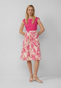 Mouwloze jurk met een felroze top en een vloeiende, knielange rok met een grote bloemenprint in tinten roze en crème.