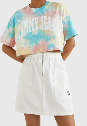 Personne portant un t-shirt court tie-dye Tommy Jeans et une jupe blanche taille haute avec fermeture éclair devant et poches plaquées.