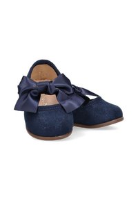 Bailarinas azul marino con un lazo de satén, fabricadas con un material suave y texturizado, con punta redondeada y suela de goma marrón.
