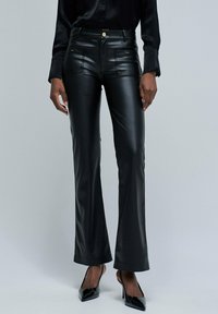 Pantalones acampanados de cuero sintético negro con bolsillos frontales, sutiles acentos de hardware dorado, diseño ajustado y textura suave y brillante.