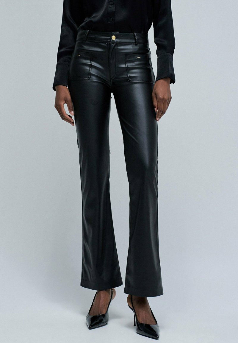 Pantalones acampanados de cuero sintético negro con bolsillos frontales, sutiles acentos de hardware dorado, diseño ajustado y textura suave y brillante.