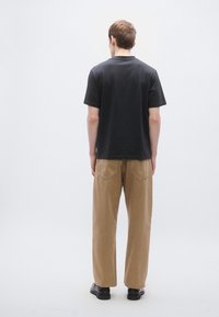 Melnas īsroku T-krekls kopā ar gaiši brūniem platām biksēm. Bikšu aizmugurē ir divas kabatas un brīvs piegriezums. Vienkāršs dizains kopumā.