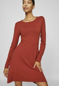 Robe à manches longues de couleur rouille en tissu côtelé, avec un décolleté rond et une silhouette évasée, dotée d'une taille cintrée et d'une texture lisse.