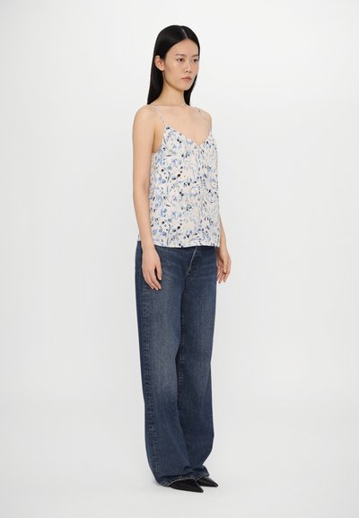 Floral-patterned light tank top with thin straps, paired with loose-fitting dark blue jeans and black pointed shoes. Plain white background.