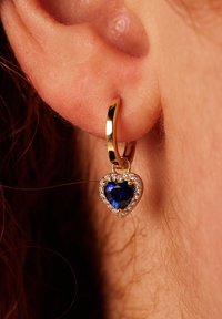 Goldene Creolen mit einem herzförmigen blauen Edelstein, umgeben von klaren Steinen, die ein poliertes Finish und einen sicheren Verschluss aufweisen.