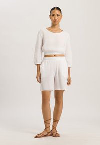 Biała, lekka, teksturowana bluzka z rękawami 3/4, połączona z pasującymi szortami. Całość dopełniają brązowe sandały gladiatorki.