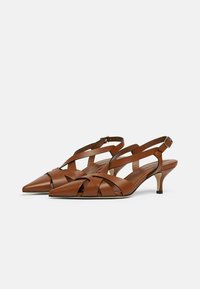 Scarpe con tacco slingback in pelle marrone con punta affusolata, cinturini intrecciati, tacco sottile e superficie liscia. Design minimalista con una silhouette elegante.