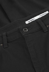 Svarta byxor i bomullsblandning med knappstängning framtill, bälteshällor och en etikett sydd på insidan av midjeresan.