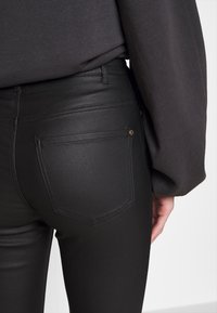 Svarta, figurnära jeans med en slät textur, som har bakfickor och minimal detaljering. Midjebandet är enkelt, utan synlig hårdvara.