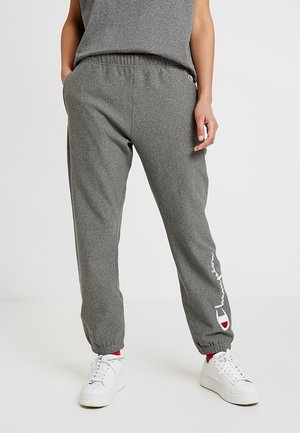 Persoon draagt grijze Champion joggingbroek met elastische boorden en logo op het linkerbeen, gecombineerd met witte sneakers en rode sokken.