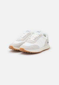 Vieglas sporta apavi ar baltu acu tīklu augšdaļu, pelēkiem zamša akcentiem un gumijas zole. Iespējas ietver baltas šnīres un mazu logotipu uz valkāšanas daļas.