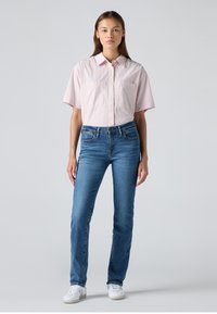 Striped short-sleeve shirt in light pink with white stripes, paired with mid-blue jeans and white sneakers, worn by a standing figure.