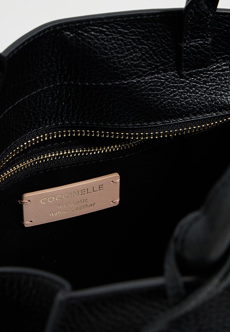 Czarna torebka skórzana o teksturowanej powierzchni z złotym zamkiem błyskawicznym. Wewnątrz znajduje się skórzana metka z napisem "Coccinelle." Gładki, trwały materiał.
