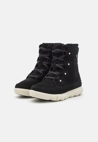 Botines de ante negros con cordones en la parte delantera, forro de piel de pelaje y suela de goma crema con bordes redondeados y superficie de agarre texturizada.