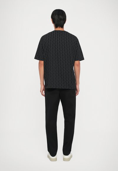 Chemise noire à manches courtes avec un motif géométrique subtil, assortie à un pantalon noir et des chaussures à semelle blanche. Texture de tissu lisse.