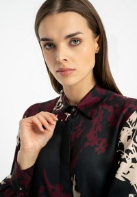 Jedwabna bluzka w czarno-kremowy wzór kwiatowy z bordowymi akcentami, z kołnierzykiem na guziki i długimi rękawami. Gładka tekstura.