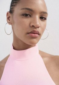 Pink ribbed halter top, with a high neckline and textured fabric. Features large silver hoop earrings against a light background.
