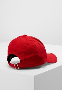 Boné vermelho de baseball feito de algodão, com aba curvada, fecho ajustável na parte de trás e ilhós bordados para ventilação. Design padrão.