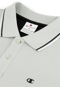 Jasnoszara koszulka polo z teksturowanej tkaniny, z czarno-białym paskowanym kołnierzykiem, trzema guzikami i małym haftowanym logo.