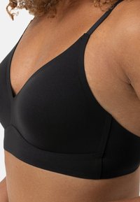 Black, soft fabric bralette with a V-neck design, adjustable straps, and seamless edges, offering a smooth silhouette.