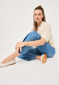 Světle krémový pletený polo s krátkým rukávem, modré široké džíny, stříbrné baleríny s béžovou podešví a řetízkový náramek na zápěstí.