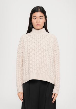 Suéter de punto cable beige claro con un cuello alto tipo mock y dobladillo acanalado. Presenta patrones texturizados y mangas largas. Combinado con una falda negra.