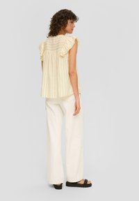 Lichtgele gestreepte top met ruffles aan de mouwen en een uitlopende achterkant, gecombineerd met off-white wijde broekpijpen en chunky zwarte sandalen.