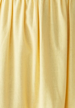 Geel stof met een fijne gaasstructuur, hangend met zachte verticale plooien en lichte schaduwen.