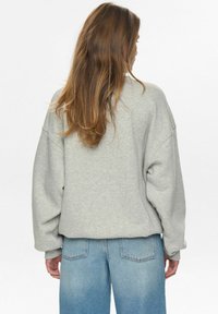 Svetlo siva oversize dukserica z nizkimi rameni, sproščenega kroja in rebrastimi manšetami, v kombinaciji s svetlo modrimi kavbojkami. Mehka tekstura.