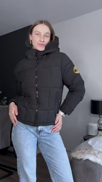 Μαύρο μπουφάν με επένδυση, με σχέδιο από χρυσωμένες ραφές, κλείσιμο με φερμουάρ, κουκούλα και κεντημένο λογότυπο στο μανίκι. Συνδυάζεται με ανοιχτό μπλε τζιν.